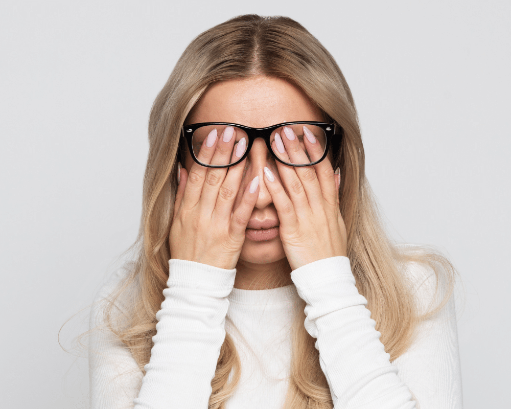 Femme blonde avec lunettes cachant son visage dans ses mains, signe de fatigue mentale ou de découragement.